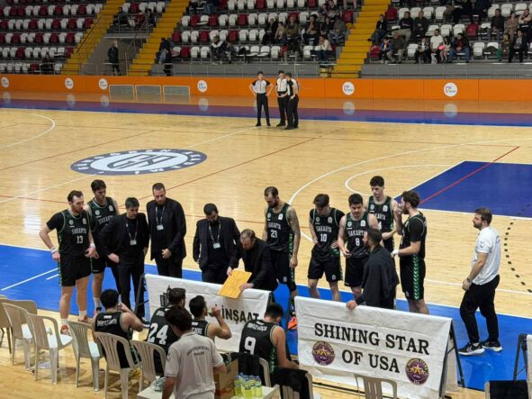 Antrenman ve maç hazırlıkları yapan basketbol ekibi, seyircilerle dolu salonda sahaya odaklanmış durumda.